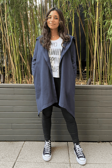 navy blue mid-length cardigan with asymmetrical hem, pockets, and hood, worn over white shirt and pants, and converse shoes