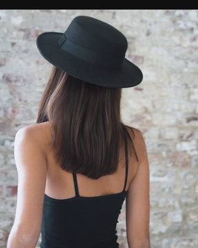 female wearing black halter neck short, fitted bodycon dress with thin shoulder straps. Also wearing black fedora hat