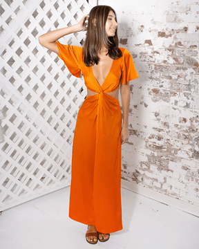 female wearing luxurious, orange hammered silk satin, full length dress with short ruffle sleeves, low front V neck, center twist design with revealing waist sides, and a low back design that has elastic at edge. Also wearing orange neck silk tie wrapped in bow