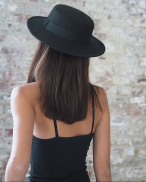 female wearing black halter neck short, fitted bodycon dress with thin shoulder straps. Also wearing black fedora hat